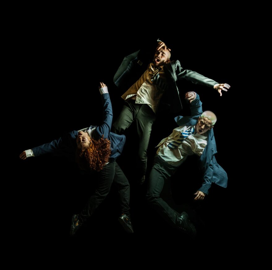 Three adult dancers in school uniform.  One jumping, the others leaning with expressive faces.