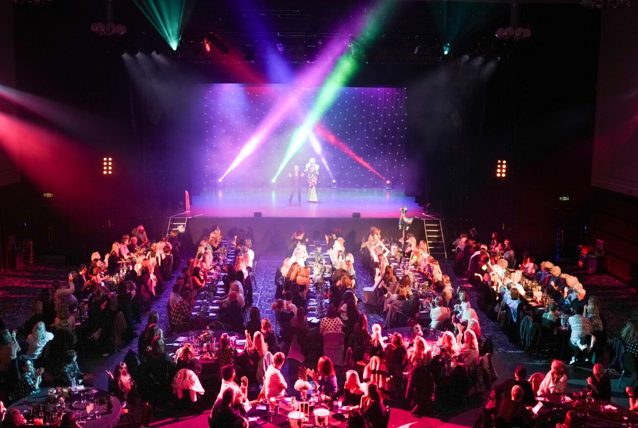 Production photograph showing the scale of Drag Bingo UK, with full tables, stage lighting and a lively audience. A great way to celebrate Christmas.